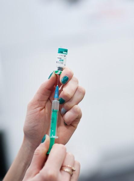 Dłoń z zielonym lakierem na paznokciach trzyma strzykawkę z igłą i fiolkę z lekiem na rozmytym tle.