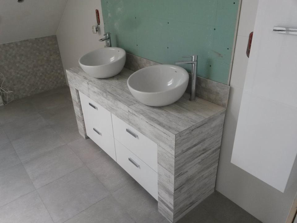 Łazienka w trakcie wykańczania: podwójna umywalka nablatowa w białych, okrągłych misach na szafce z białymi frontami i blatem imitującym drewno, szara płytka podłogowa, ściana z płyt...