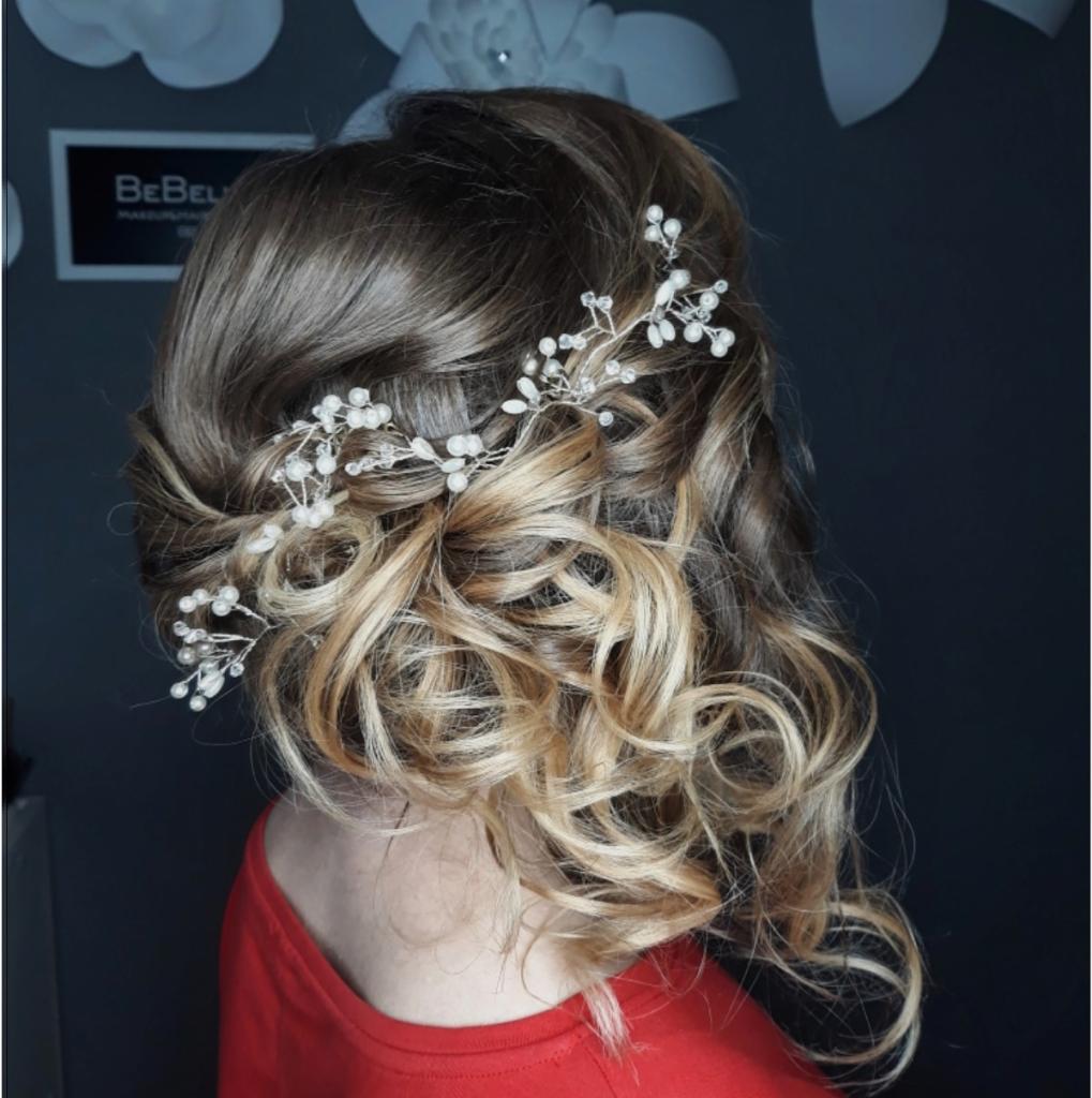 Upięcie włosów w loki z ozdobną spinką z perełkami, widok z tyłu na ciemnym tle z dekoracjami.