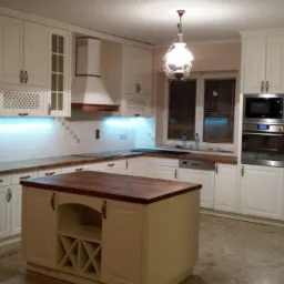 Jasna kuchnia z drewnianymi blatami, wyspą kuchenną z winiarką i oświetleniem LED podszafkowym.