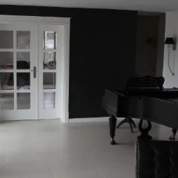 Nowoczesne, białe, dwuskrzydłowe drzwi z przeszkleniami w jasnym wnętrzu z czarną ścianą w kwiaty i czarnym fortepianem