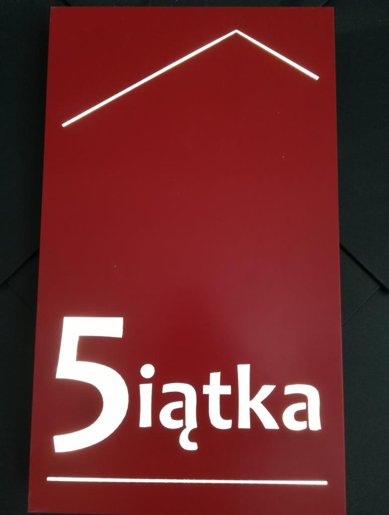 Czerwona tabliczka z białym napisem '5iątka' i uproszczonym symbolem domu, prawdopodobnie logo firmy.