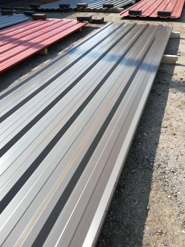 Profiled metal sheets in silver and red, stacked on wooden supports, ready for installation on a roof.