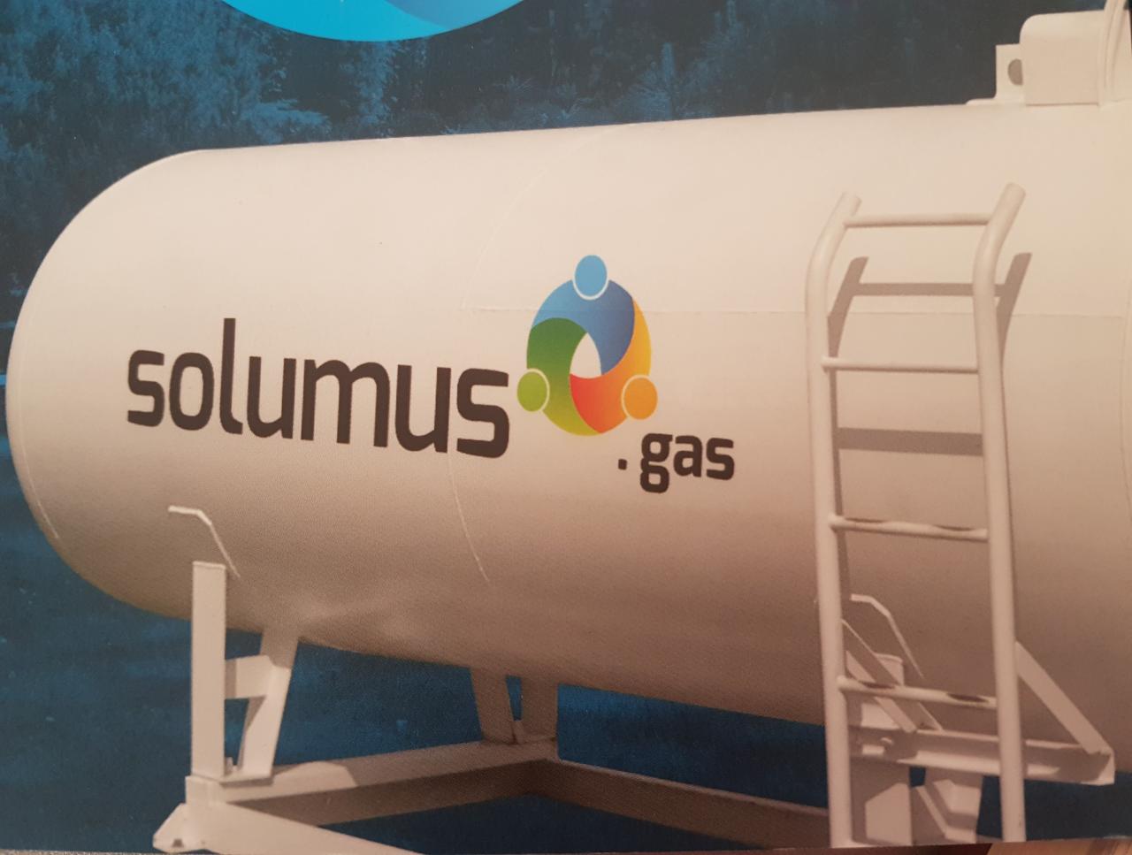 Biały zbiornik z logo 'solumus .gas' i drabinką, na tle niebieskiego tła z motywem lasu.
