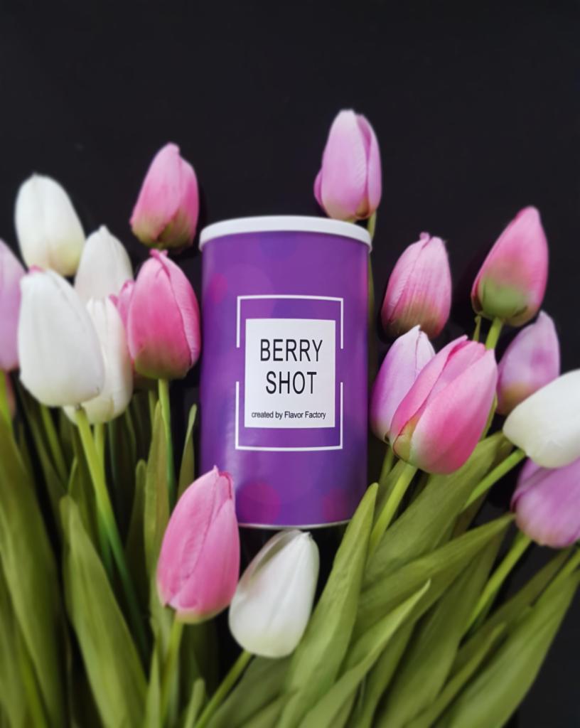 Fioletowa puszka z napisem 'Berry Shot' otoczona bukietem białych i różowych tulipanów na czarnym tle.