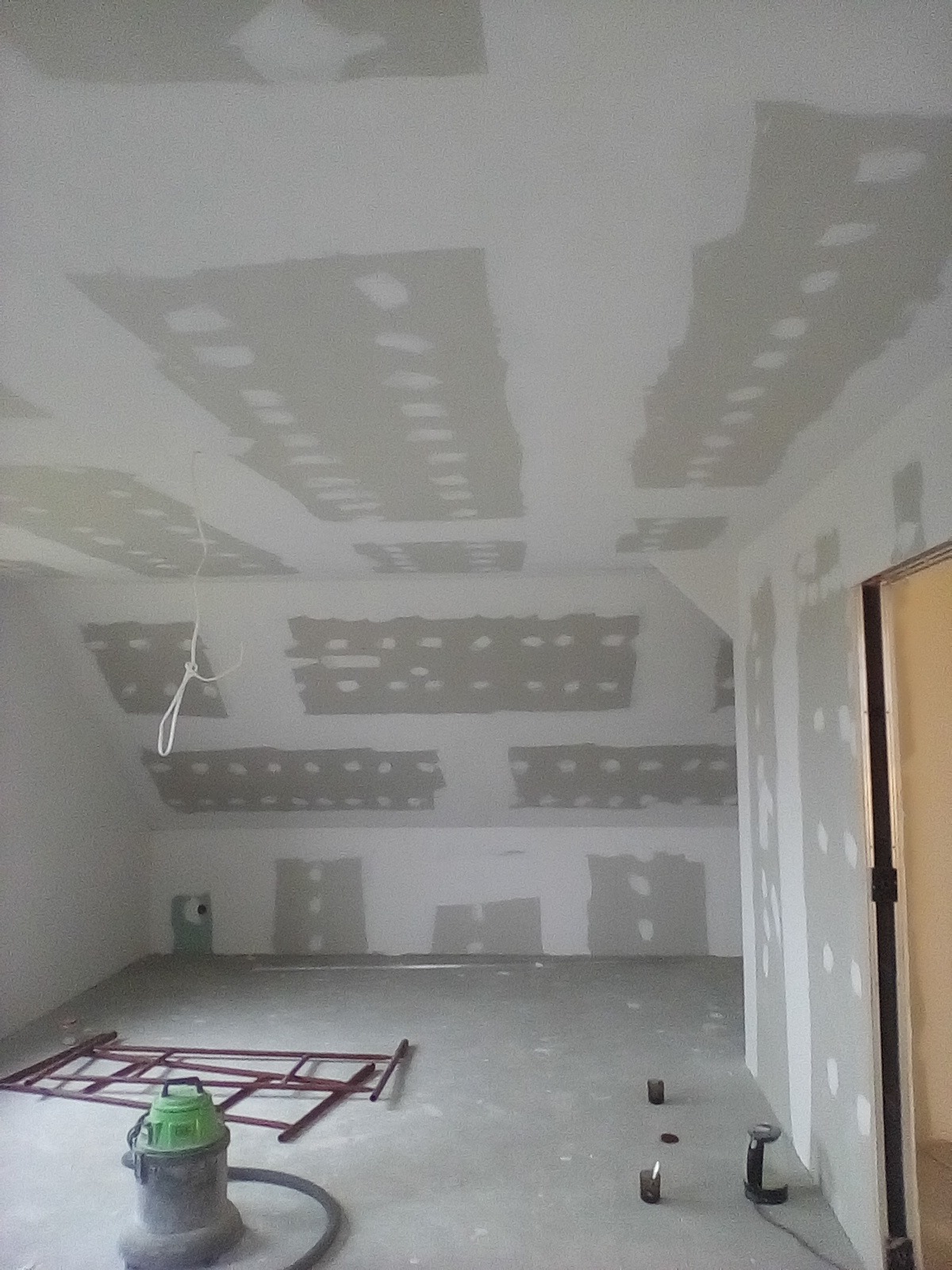 Montaż płyt gipsowo-kartonowych na skosach poddasza, widoczne łączenia szpachlowane, drabina malarska i odkurzacz przemysłowy na posadzce.