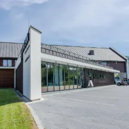 Budynek firmy Kameleon.pro w Kalwarii Zebrzydowskiej z dużym parkingiem, widok z zewnątrz na przeszklone wejście i logo firmy.