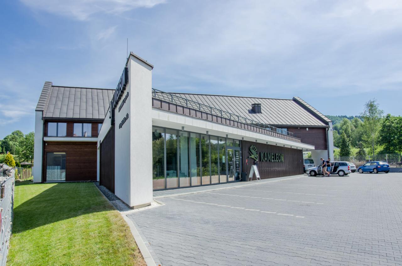 Budynek firmy Kameleon.pro w Kalwarii Zebrzydowskiej z dużym parkingiem, widok z zewnątrz na przeszklone wejście i logo firmy.