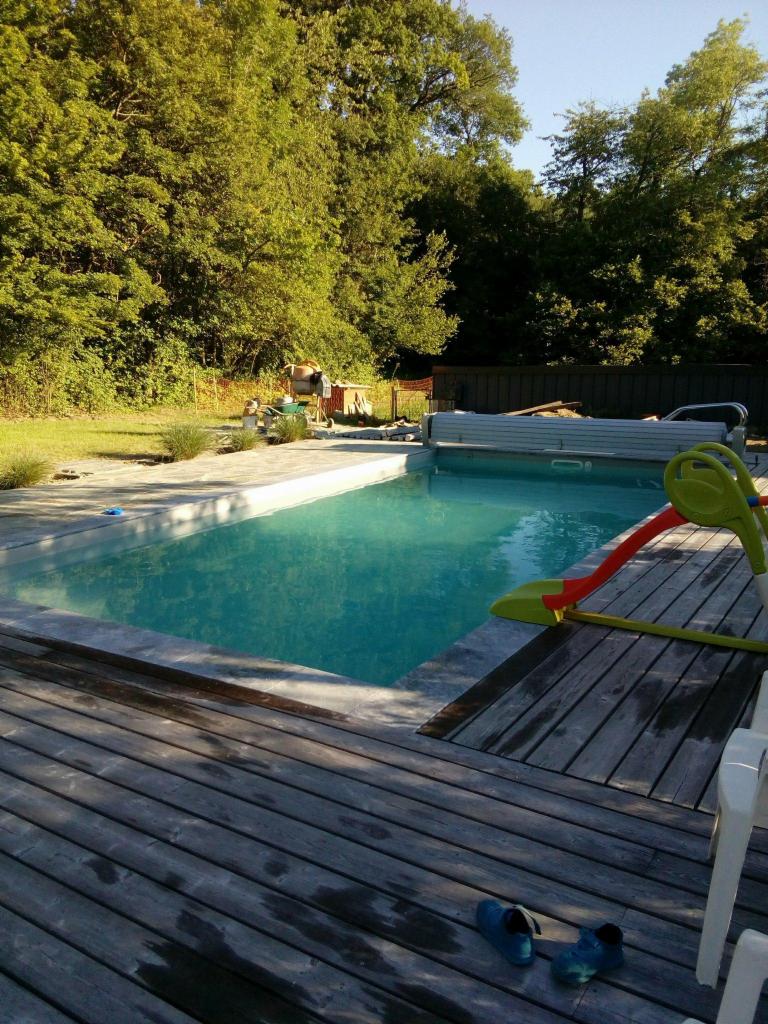 Basen ogrodowy z drewnianym tarasem, zjeżdżalnią dla dzieci i niebieskimi butami na deskach.