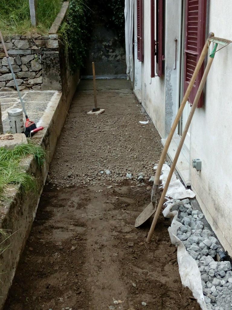 Przygotowanie terenu pod ścieżkę w ogrodzie w miejscowości Pisz: wyrównana ziemia, rozsypany żwir, narzędzia ogrodnicze oparte o ścianę budynku.