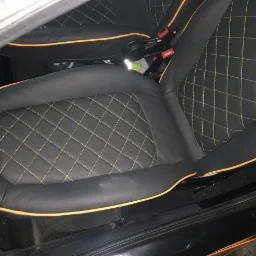 Czarna skórzana tapicerka samochodowa z żółtymi przeszyciami w romby i pomarańczowym obszyciem.