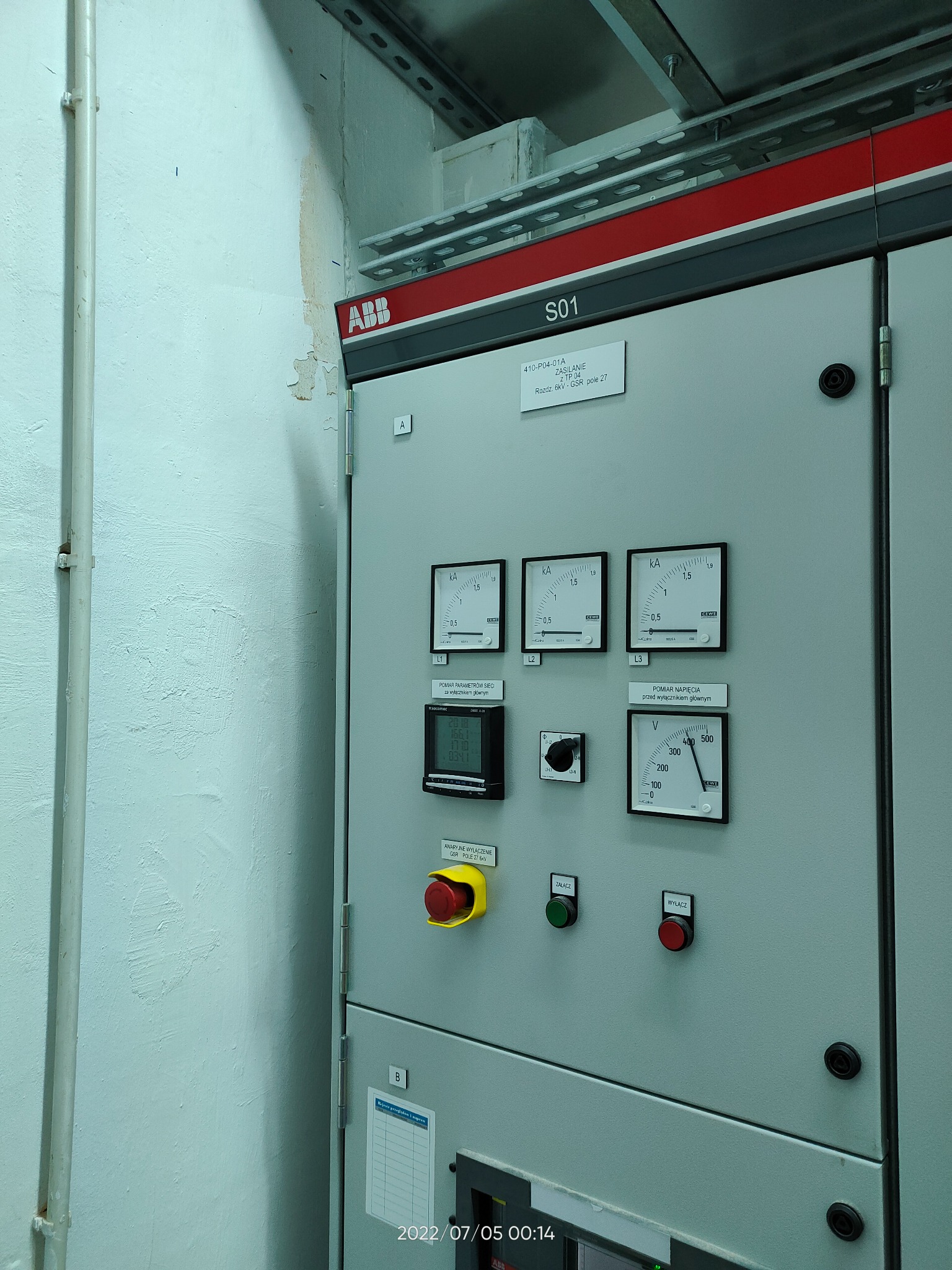 Szara szafa sterownicza ABB z analogowymi miernikami prądu i napięcia, przyciskami załącz/wyłącz oraz opisami technicznymi, umieszczona w pomieszczeniu technicznym.