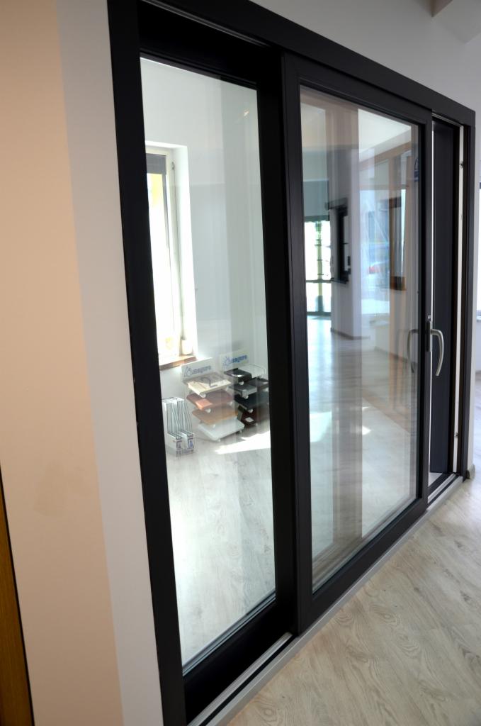 Nowoczesne przesuwne drzwi szklane z czarną ramą, widok z boku, w tle ekspozycja próbek materiałów.