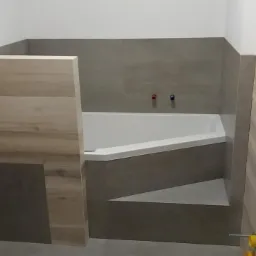 Wykończona łazienka z narożną wanną obudowaną szarymi płytkami, z elementami wykończenia imitującymi drewno oraz widocznymi przyłączami wodnymi z czerwonym i niebieskim zaworem.