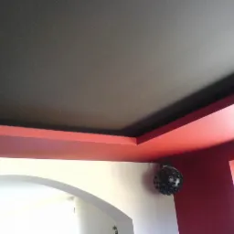 Dwupoziomowy sufit z czarną wnęką i czerwoną ramą, widoczna lampa dekoracyjna w kształcie kuli z otworami.