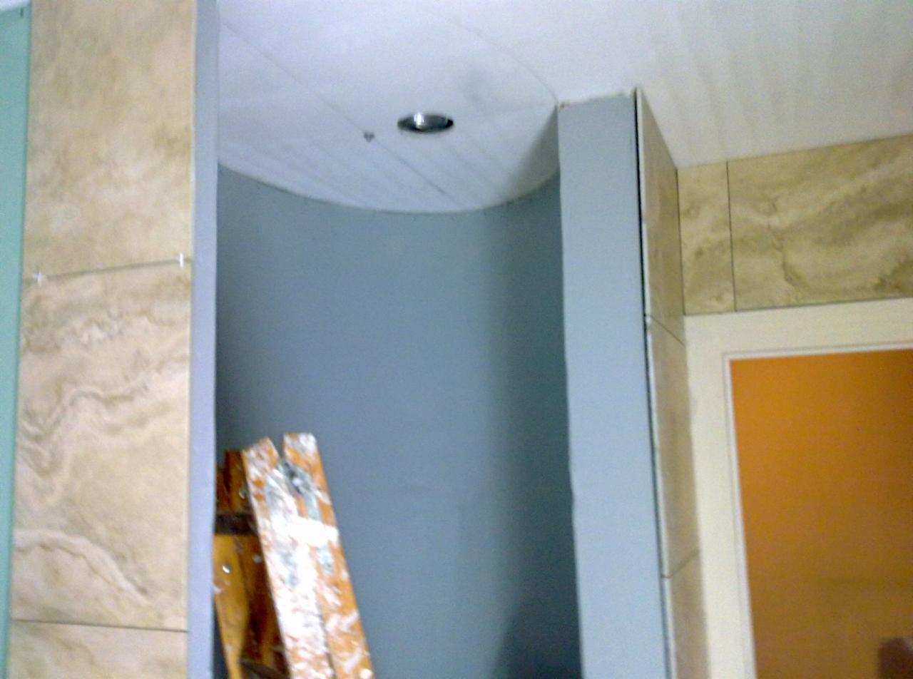 Wnętrze łazienki w trakcie prac wykończeniowych, widoczna drabina oparta o ścianę, częściowo wykończona ściana z płytek imitujących marmur i sufit z wbudowanym oświetleniem.