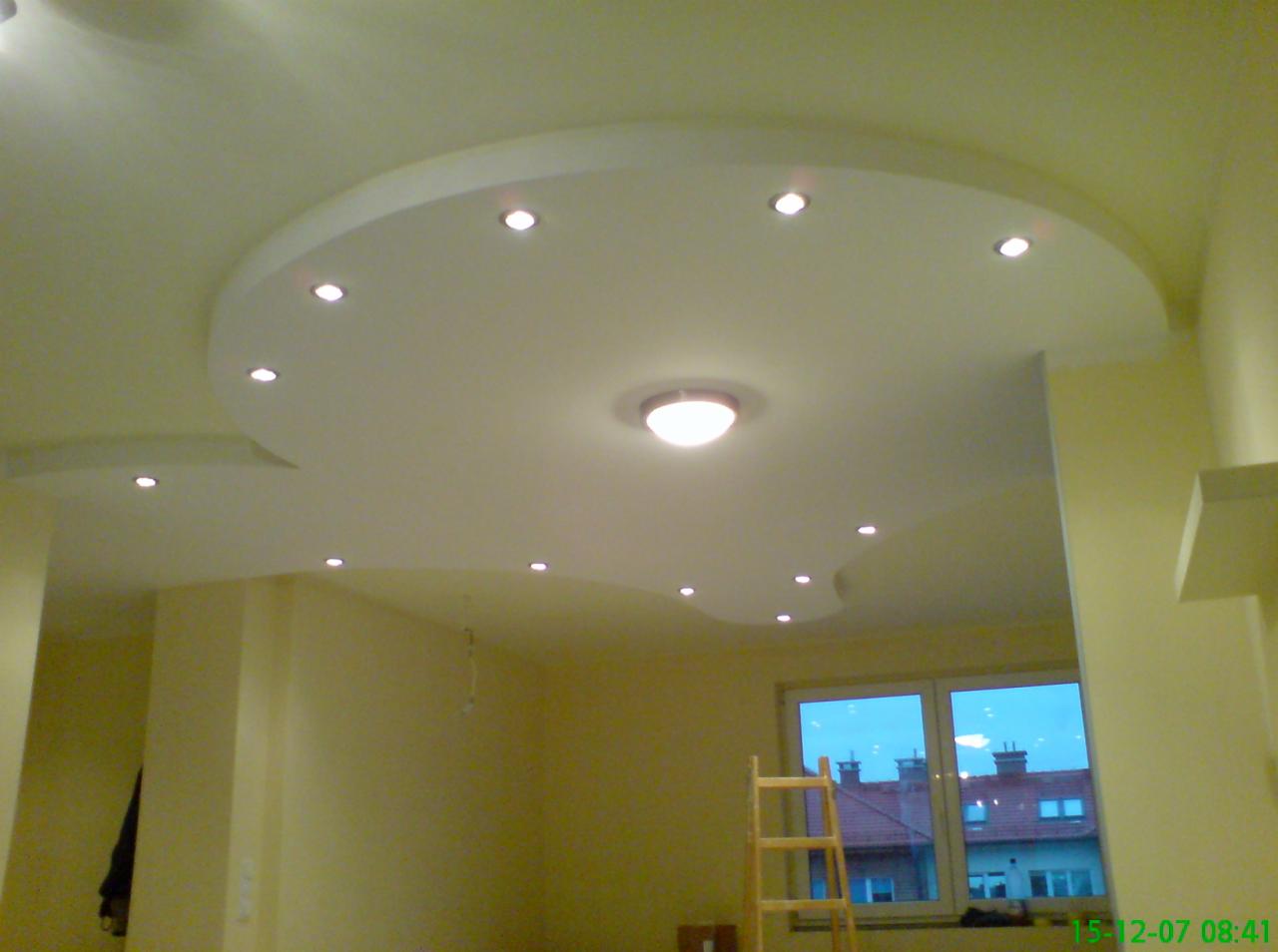 Wykończony sufit podwieszany z oświetleniem punktowym i centralnym, widok z dołu, w tle okno i drabina.