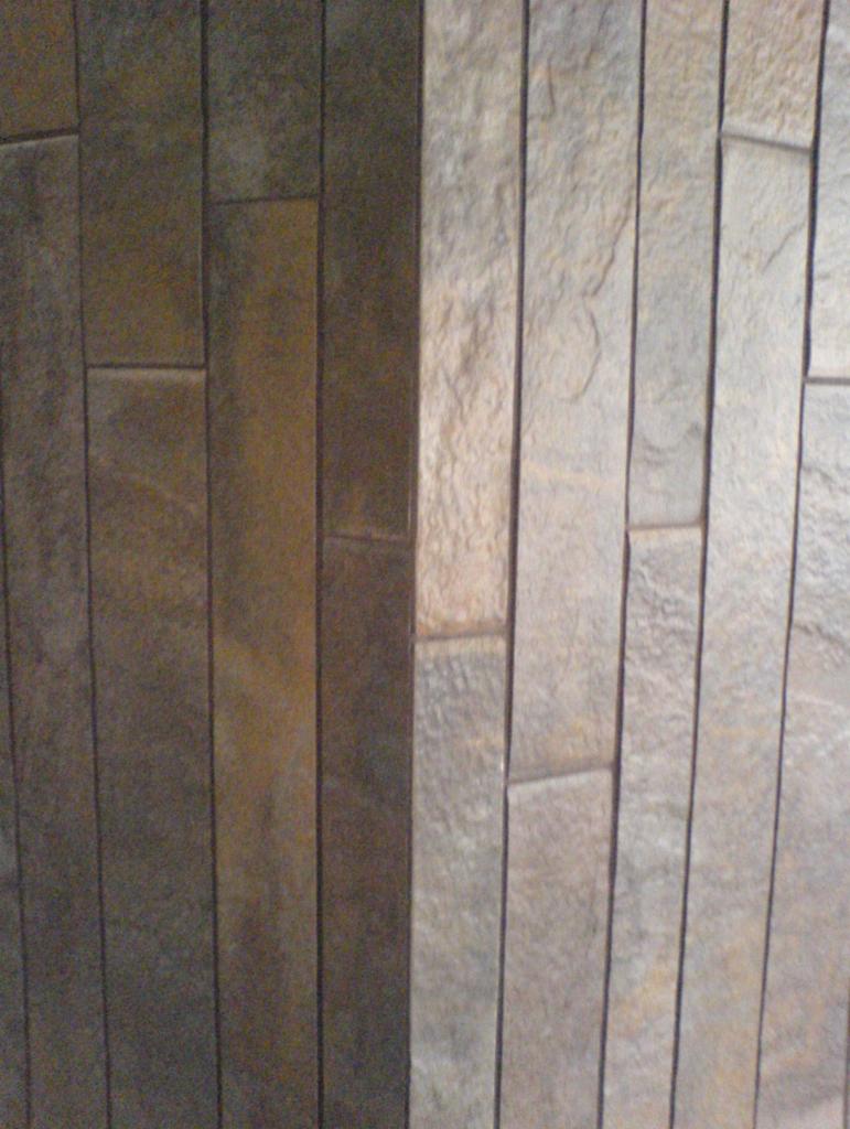 Fragment ściany wykończonej pionowymi panelami w dwóch odcieniach brązu i beżu, z widoczną fakturą kamienia.