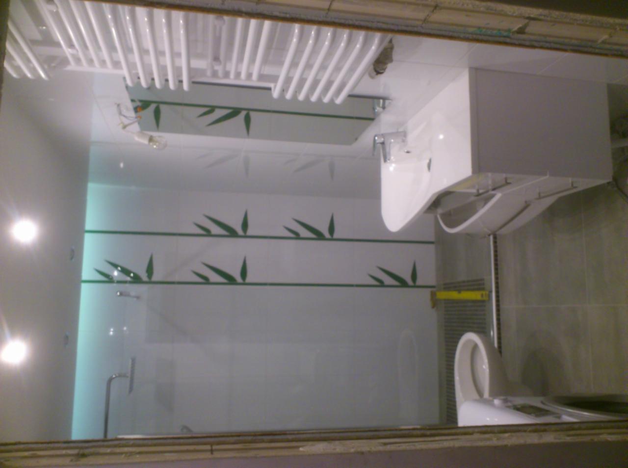 Wykończona łazienka w Gdyni z białymi płytkami zdobionymi zielonym motywem bambusa, widoczna umywalka z szafką, grzejnik drabinkowy i toaleta.