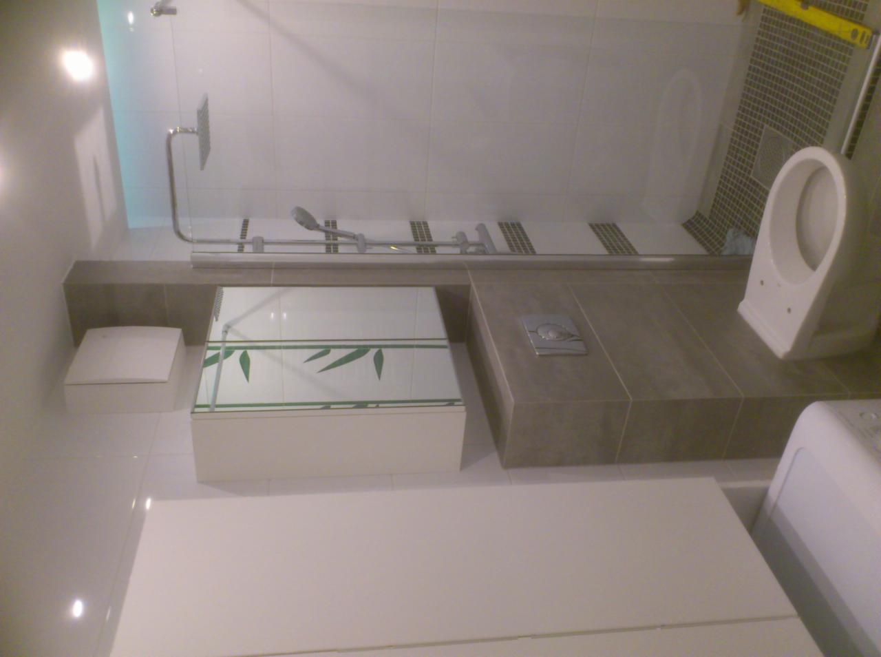 Nowoczesna łazienka po remoncie z kabiną prysznicową, toaletą wiszącą i zabudową szafki pod umywalkę z motywem bambusa na płytkach.