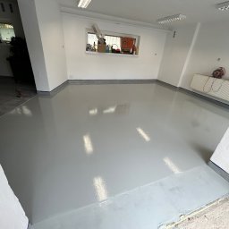 BUD-ART - Świeżo wylana, błyszcząca, szara posadzka żywiczna w pomieszczeniu z białymi ścianami i oknem z narzędziami na parapecie.