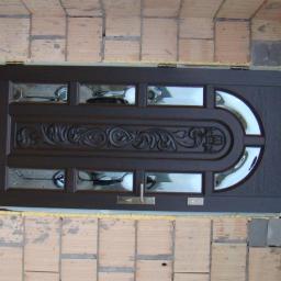 PHU Budoplast - Brązowe drzwi wejściowe z dekoracyjnym wzorem i szybami, w trakcie montażu, widoczne cegły i pianka montażowa.