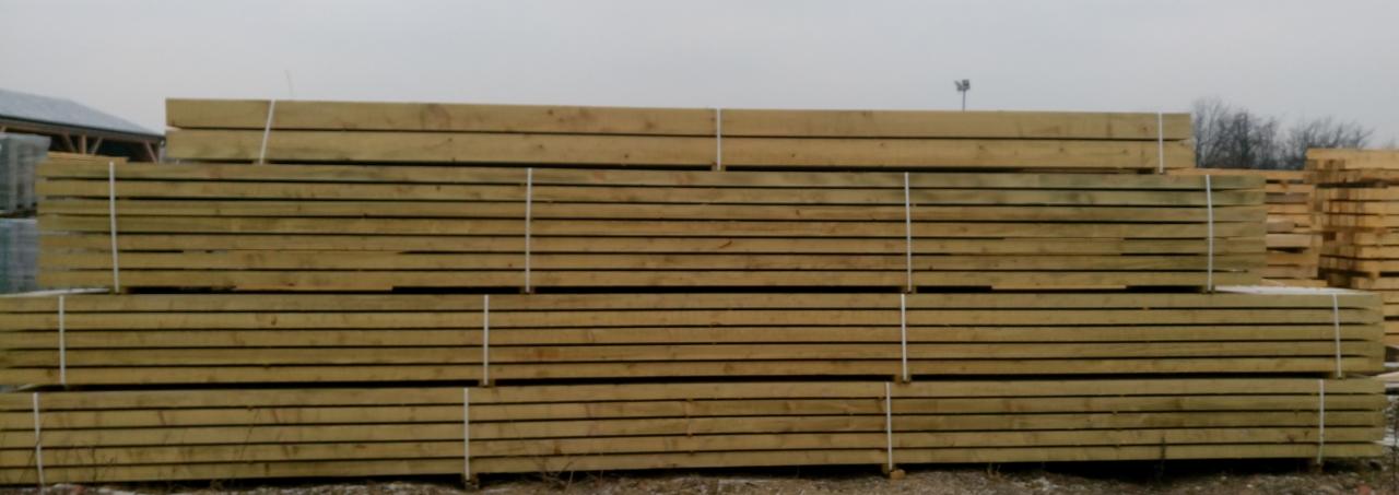 Stosy świeżo przetartej tarcicy budowlanej, zabezpieczone białym sznurkiem, składowane na zewnątrz w pochmurny dzień.