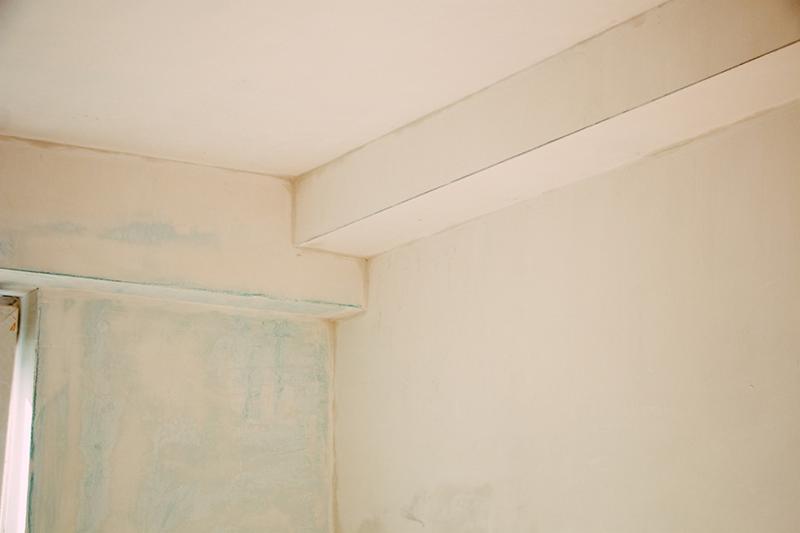 Przygotowana do malowania ściana z widocznymi śladami szpachlowania i zaznaczeniami, z zamontowaną listwą sufitową.