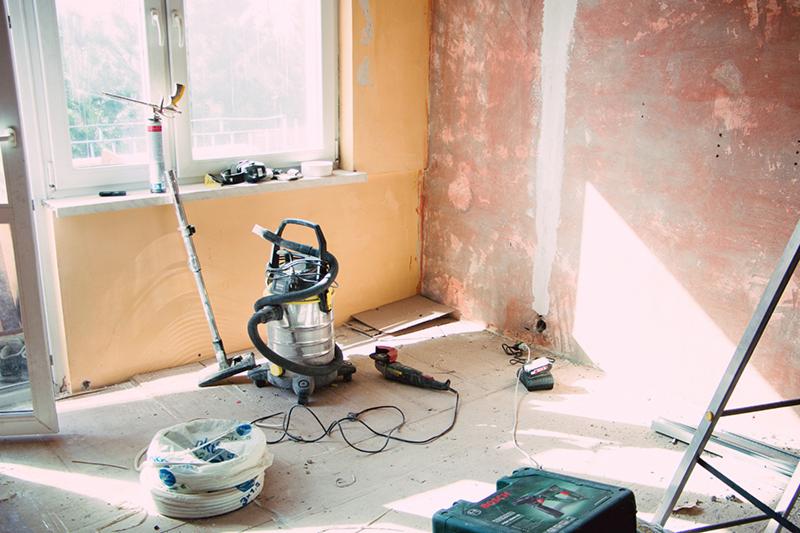 Pokój w trakcie prac przygotowawczych w Rzeszowie, z widocznymi ścianami po usunięciu starej farby, narzędziami budowlanymi, odkurzaczem przemysłowym i drabiną.