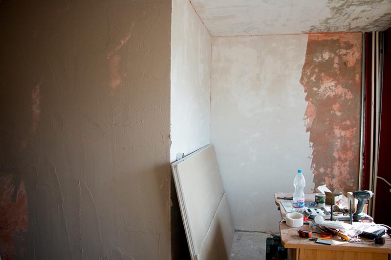 Fragment pokoju w trakcie prac wykończeniowych: ściana pokryta świeżą gładzią, płyty kartonowo-gipsowe oparte o ścianę, stół z narzędziami i materiałami budowlanymi.