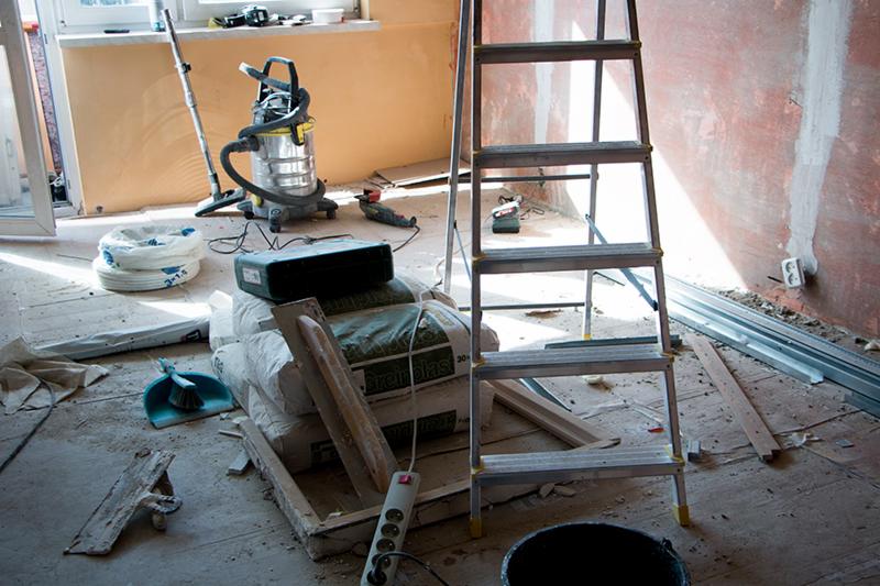 Remontowany pokój z workami gładzi, drabiną aluminiową, odkurzaczem przemysłowym i listwami przypodłogowymi.