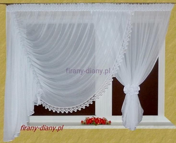 Delikatna, biała, woalowa zasłona z falbanami i koronkowym wykończeniem, upięta dekoracyjnym kwiatem, na tle okna z brązowymi ramami i bukietem czerwonych kwiatów na parapecie.