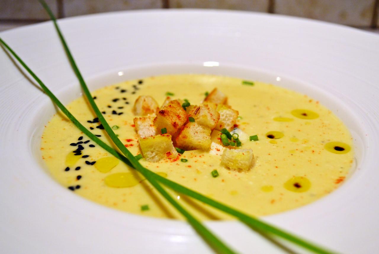 Kremowa zupa w białym talerzu, udekorowana grzankami posypanymi papryką, czarnuszką, szczypiorkiem i trzema łodygami szczypiorku.