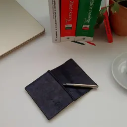 Biurko z laptopem Dell, notatnikiem ze srebrnym długopisem, kubkiem czarnej kawy i książkami prawniczymi Zbiór Karny i Zbiór Cywilny oraz roślina w doniczce.