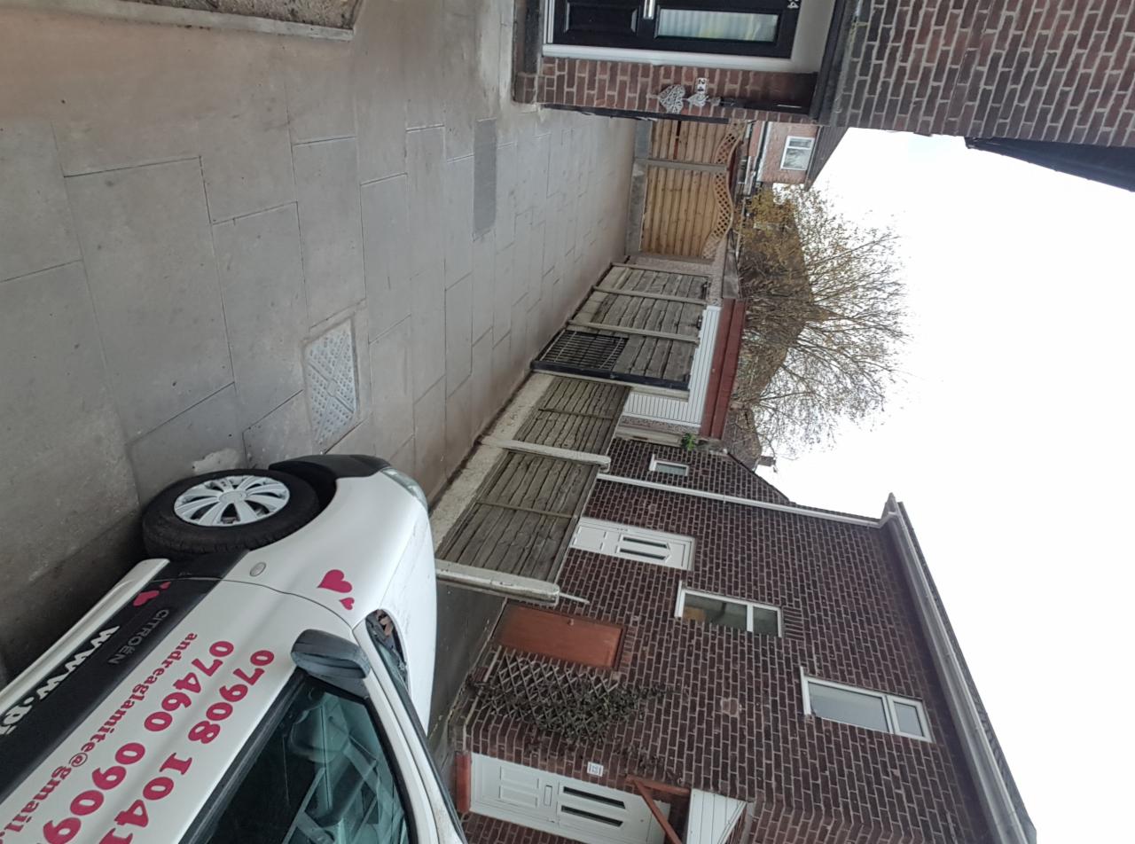 Nowo ułożona, szara kostka brukowa na podjeździe przed domem z czerwonej cegły, widoczny samochód dostawczy z numerem telefonu firmy brukarskiej.