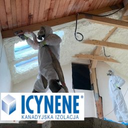 Izo Concept Sp. z o.o. - Prace izolacyjne poddasza: aplikacja białej piany natryskowej przez dwóch pracowników w kombinezonach ochronnych, widoczne drewniane elementy konstrukcji dachu.