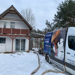 Izo Concept Sp. z o.o. - Ocieplanie pianką PUR: biały dom w zimowej scenerii, obok zaparkowany van z reklamą firmy IzoConcept i wężami do natrysku pianki. Widoczny etap przygotowania do ocieplenia.