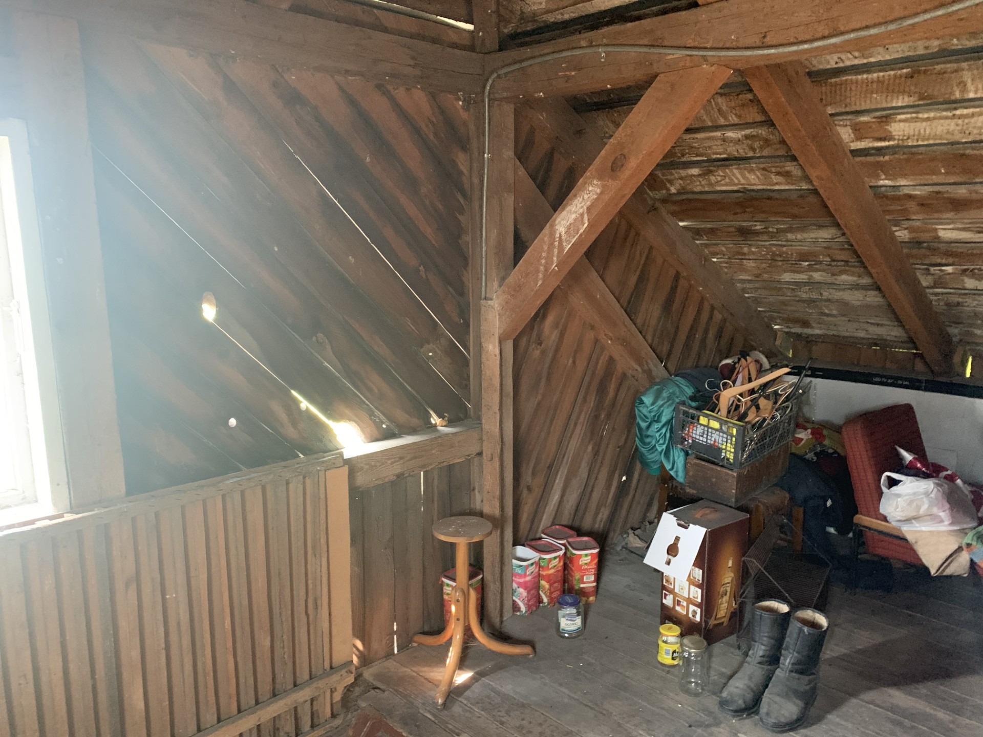 Drewniane poddasze z widoczną konstrukcją dachu przed pracami izolacyjnymi. Widoczne elementy wyposażenia i okno wpadające światło.