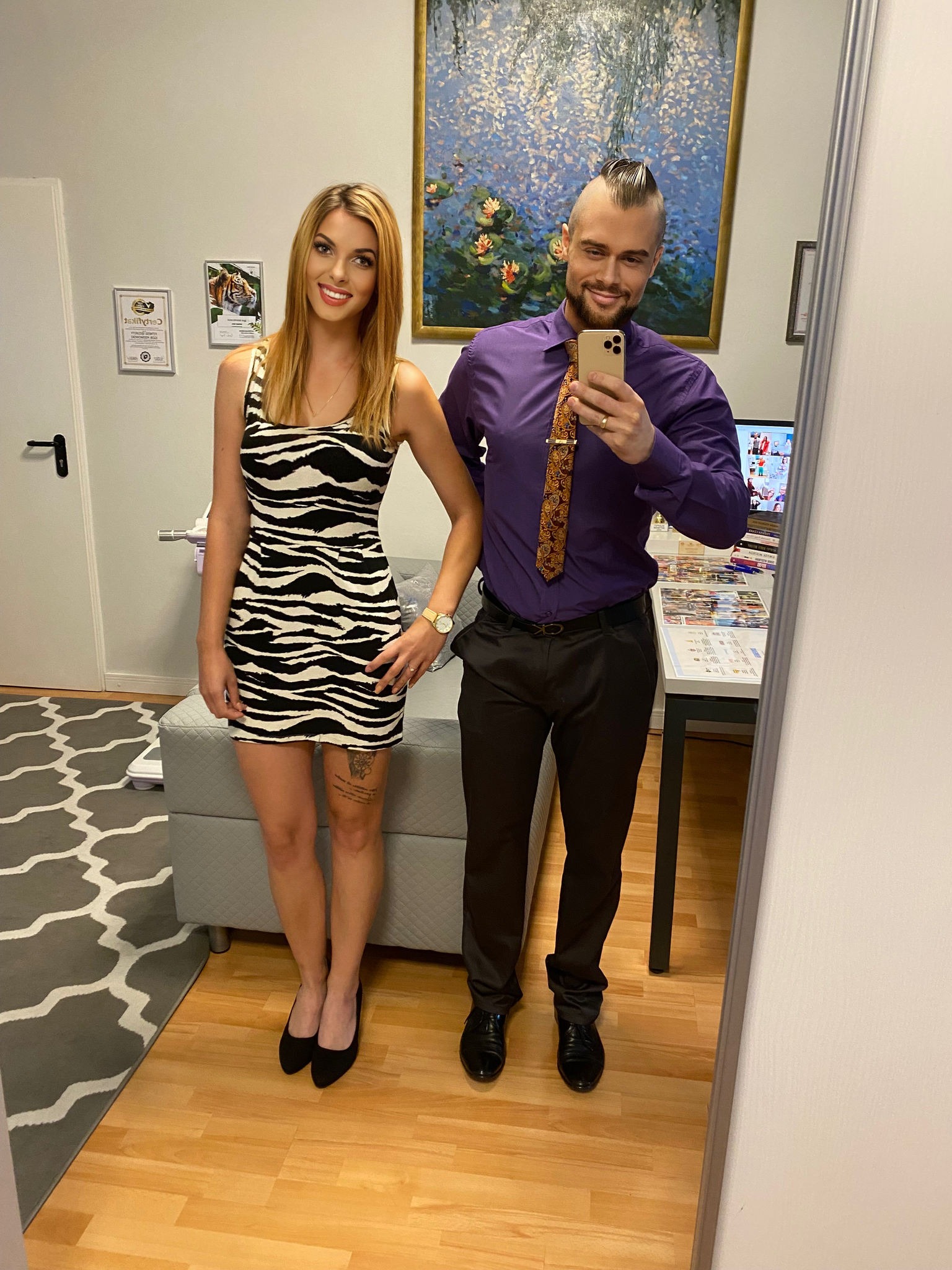 Dietetyk pozuje z klientką w sukience w zebrę, trzymając telefon przed lustrem; w tle obraz z liliami wodnymi i certyfikat na ścianie.