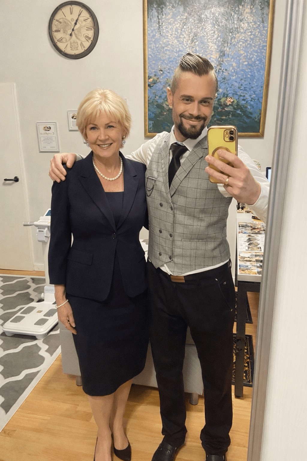 Uśmiechnięty dietetyk robi selfie z klientką w gabinecie. W tle waga diagnostyczna, zegar i obraz. Profesjonalny wizerunek budujący zaufanie.