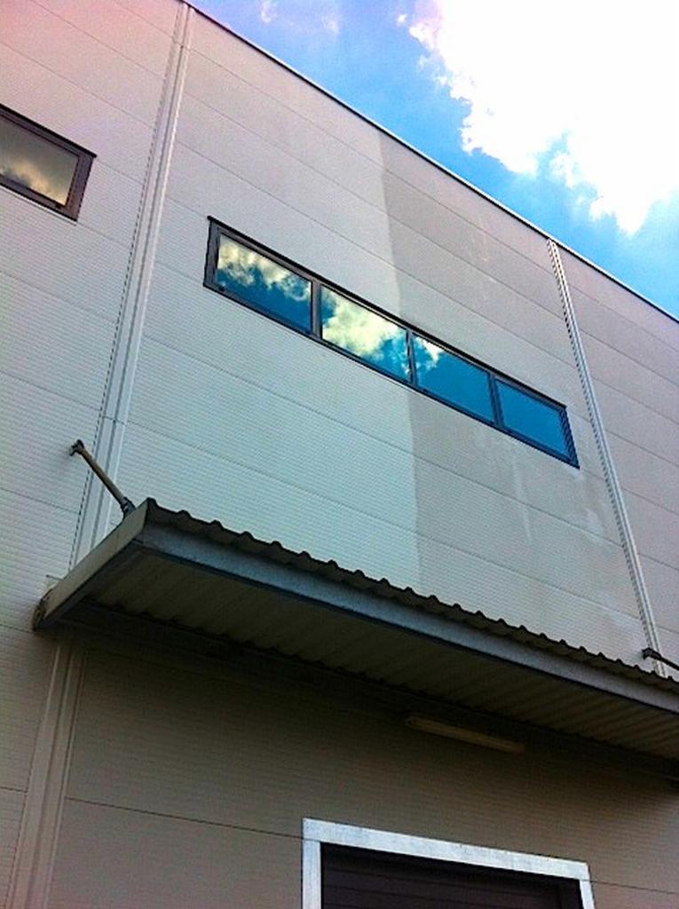 Częściowo umyta elewacja budynku przemysłowego z oknami, widoczna różnica w kolorze między czystą a brudną powierzchnią.