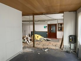 Wnętrze w trakcie demontażu ściany działowej, widoczne pozostałości po konstrukcji, gruz i elementy instalacji elektrycznej, sufit z boazerii.