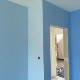 Pomieszczenie po malowaniu ścian na dwa odcienie niebieskiego, widoczna puszka instalacyjna w ścianie oraz fragment pomieszczenia obok z widoczną drabiną