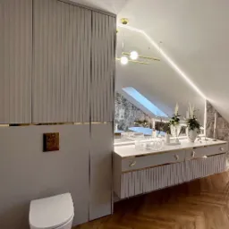 Elegancka łazienka na poddaszu ze skośnym sufitem, z zabudowaną szafą, wiszącą toaletą, umywalką wpuszczoną w blat z marmuru, złotymi akcentami i oświetleniem LED.
