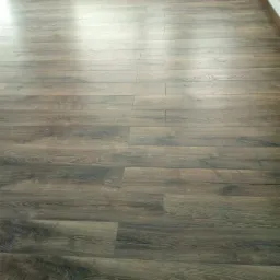 Ułożone panele podłogowe w odcieniach brązu, widoczne listwy przypodłogowe i grzejnik w tle.