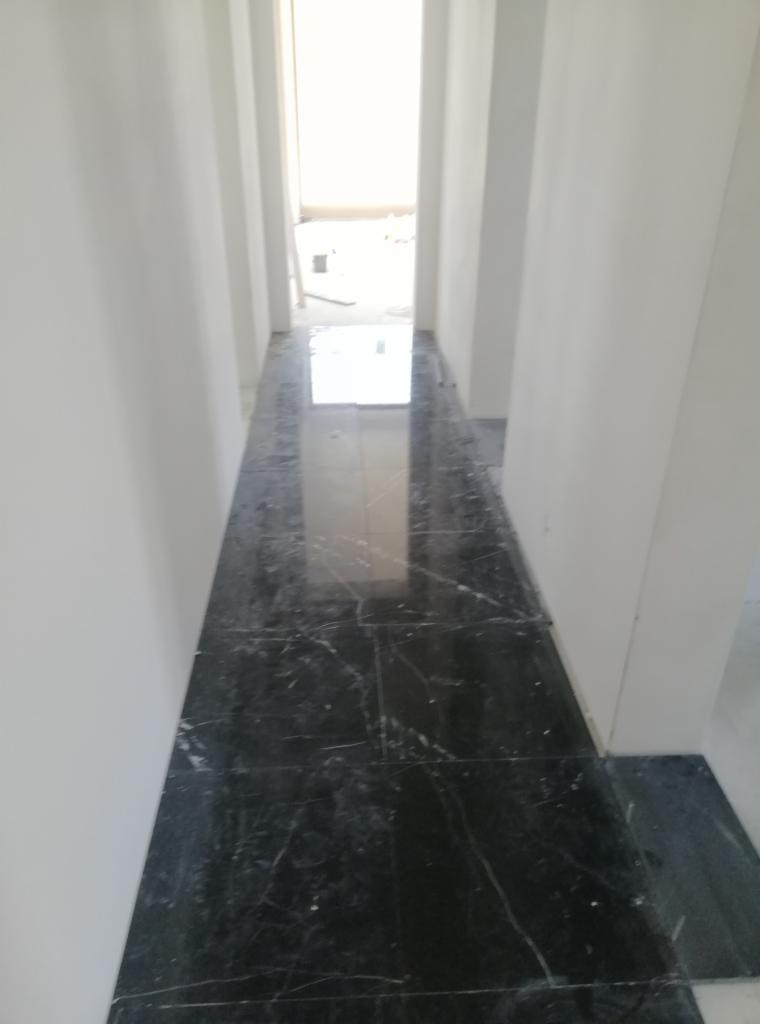 Położona, ciemna, błyszcząca marmurowa posadzka w korytarzu z białymi ścianami, widok z góry na wprost.