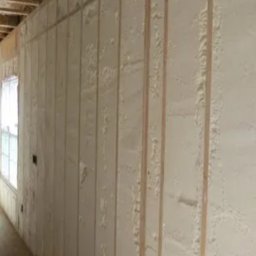 SCANDIPUR SPÓŁKA Z OGRANICZONĄ ODPOWIEDZIALNOŚCIĄ - Ściana wewnętrzna w trakcie izolacji pianką poliuretanową, widoczne drewniane listwy konstrukcyjne i nierównomiernie nałożona warstwa piany.