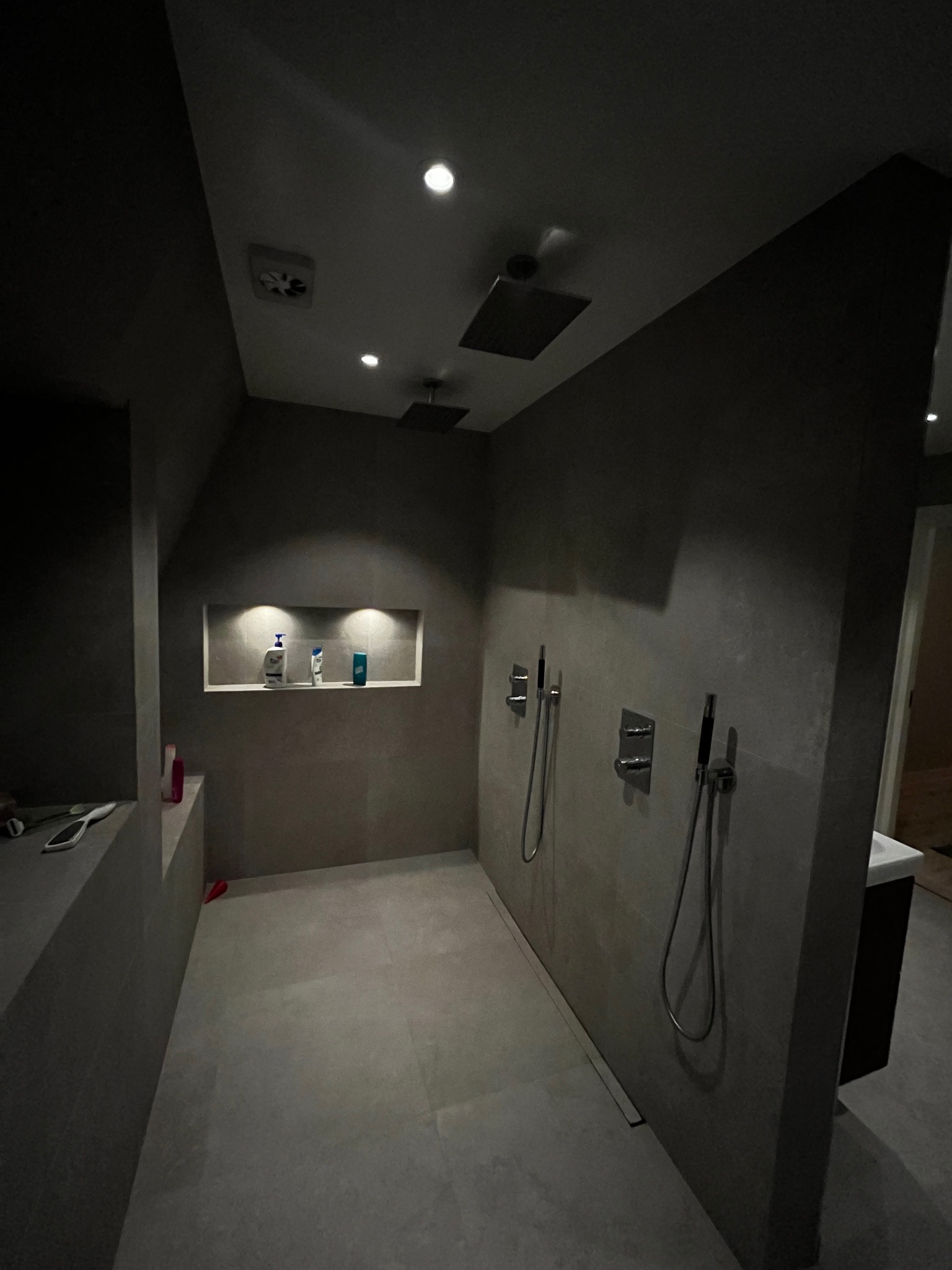 Nowoczesna kabina prysznicowa z deszczownicą, szare płytki, wnęka z podświetleniem i kosmetykami, minimalistyczne baterie.