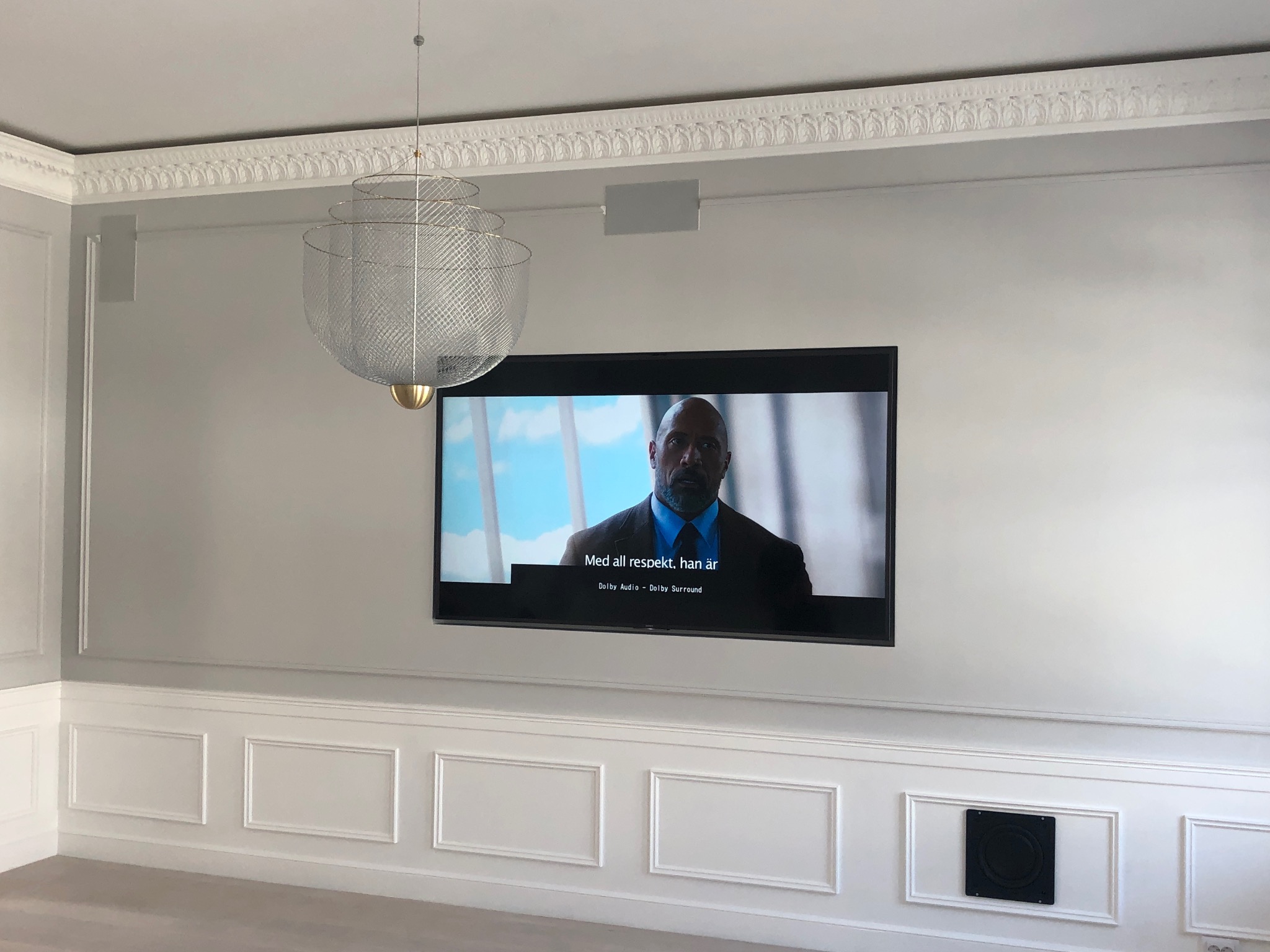 Eleganckie wnętrze z telewizorem zawieszonym na ścianie z dekoracyjną sztukaterią i nowoczesną lampą wiszącą