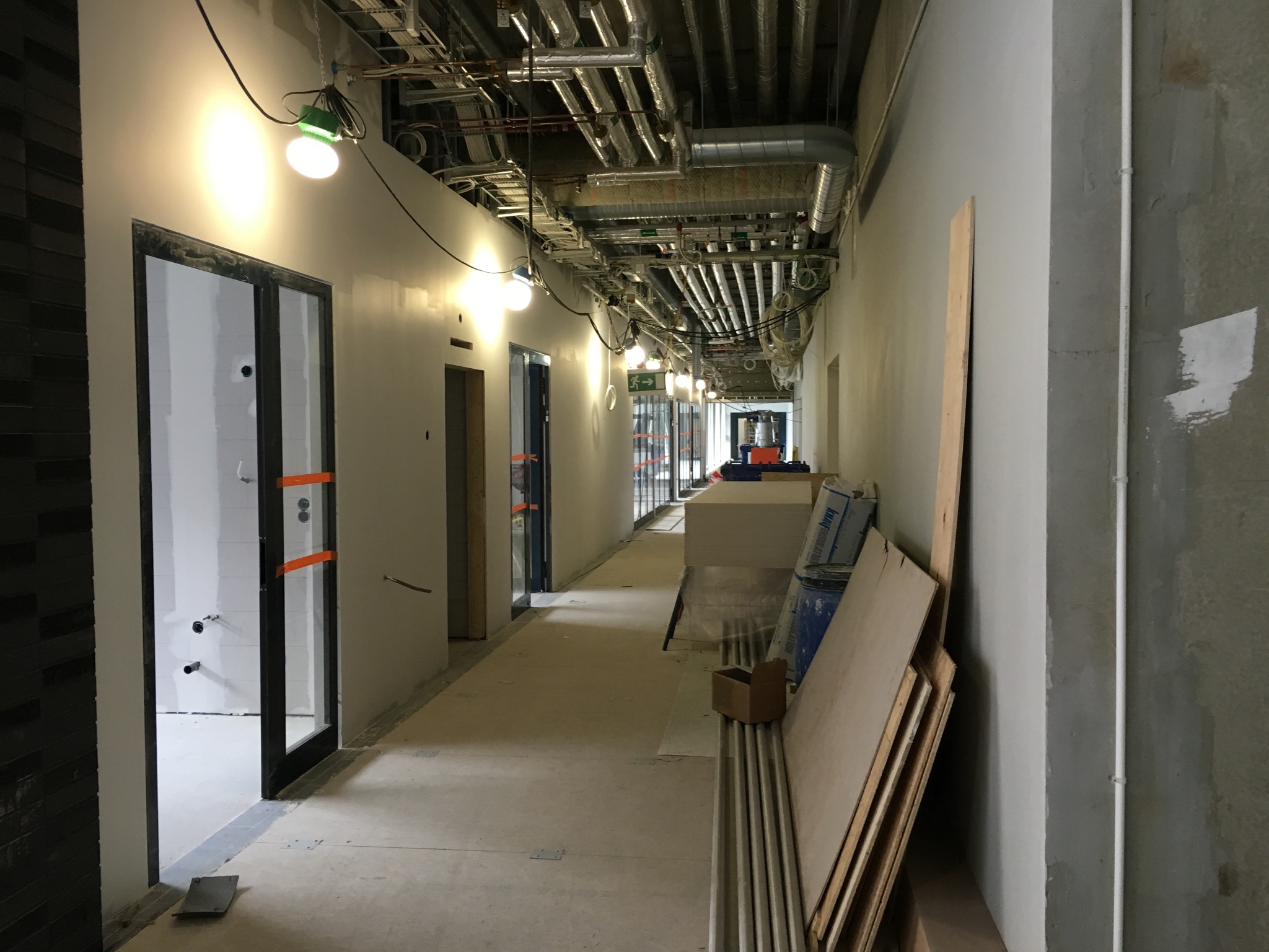 Korytarz w trakcie remontu: widoczne instalacje pod sufitem, przygotowane ściany do malowania, drzwi wstawione, płyty karton gips i materiały budowlane ułożone wzdłuż ściany.